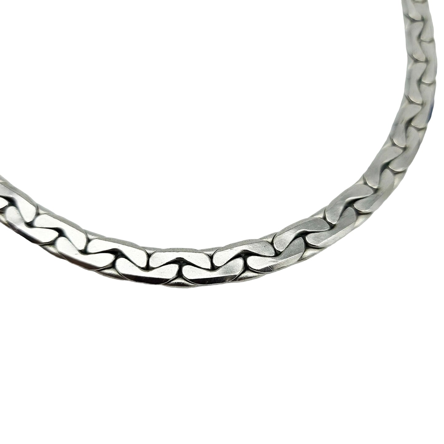 A close-up of a silver-toned metal chain necklace with a wavy, interlocking link design, photographed against a plain light gray background.